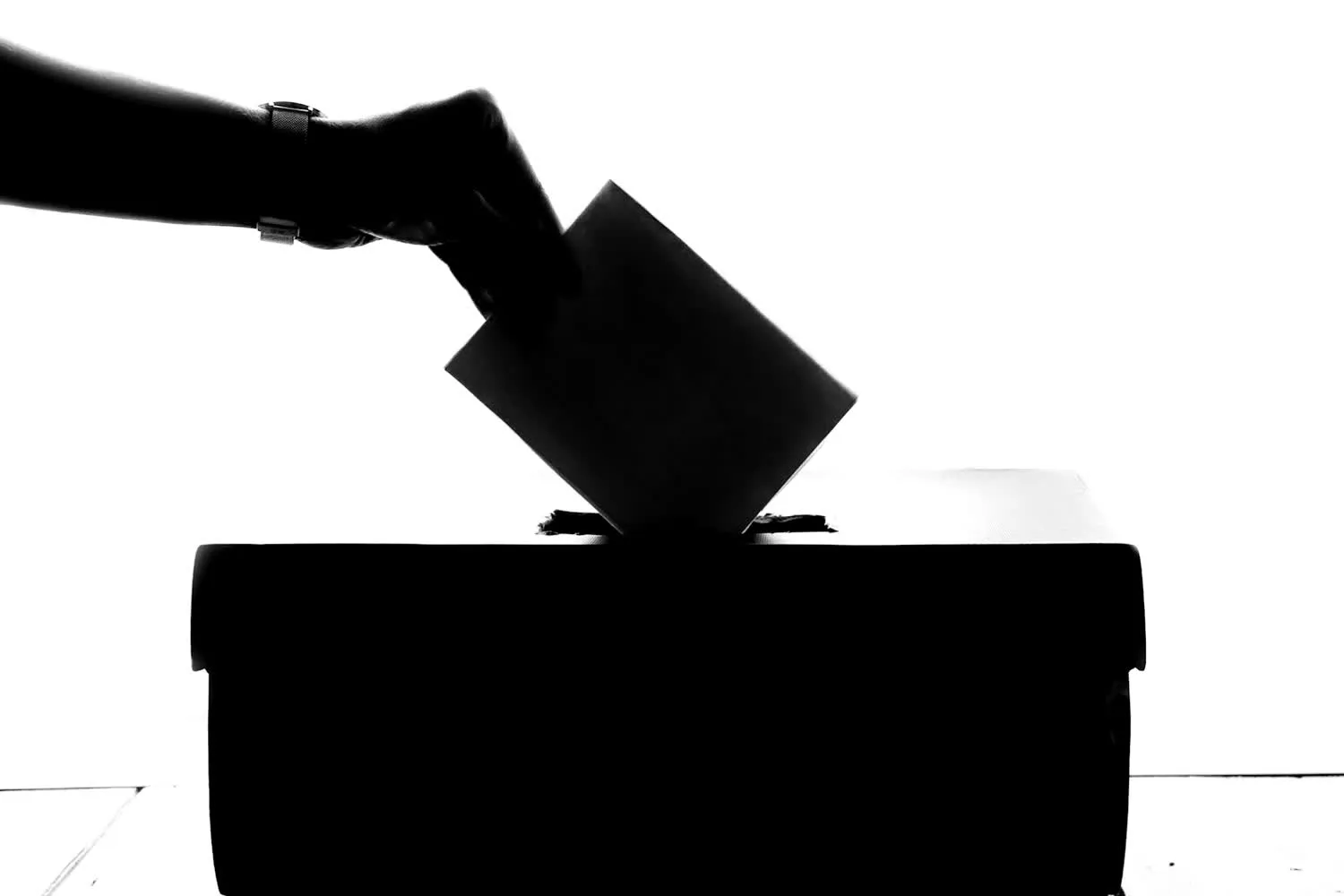 A hand dropping a paper ballot into a ballot box